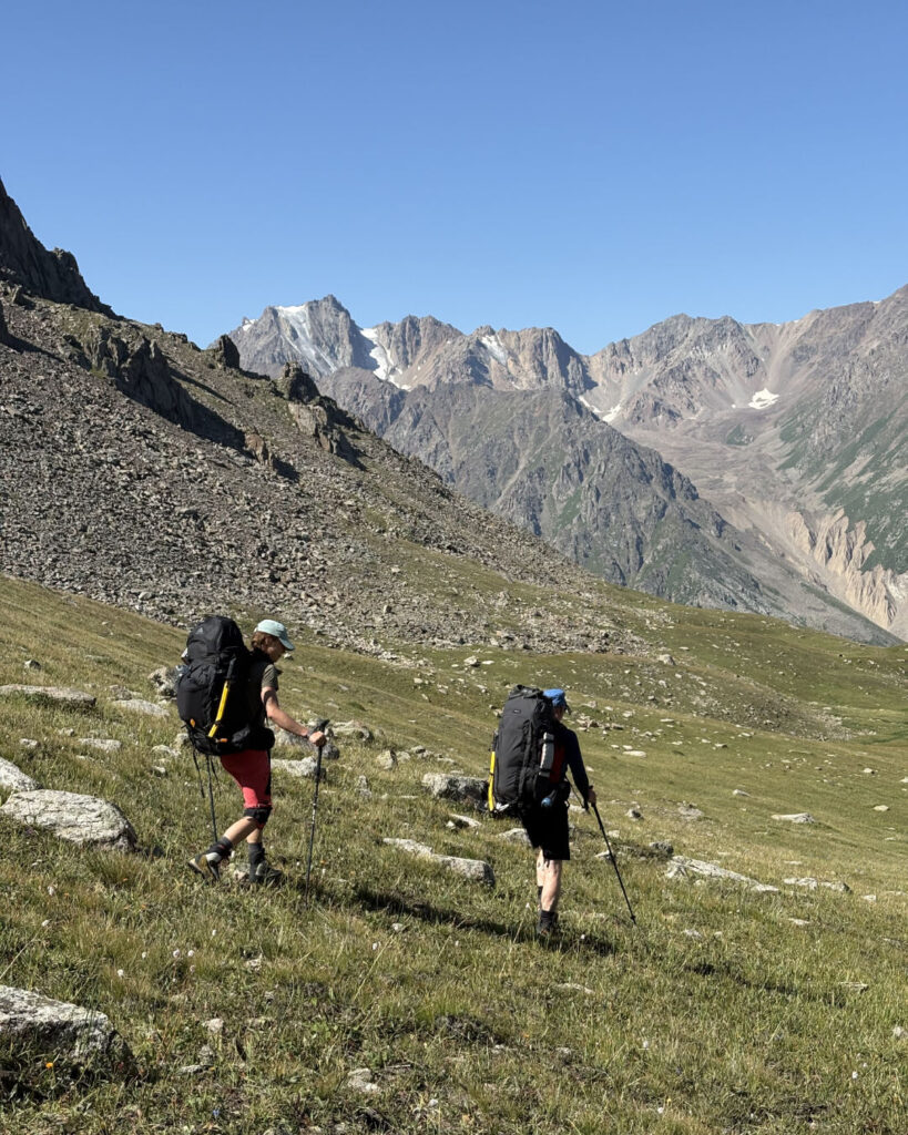 Two mountaineers descending down the grassy slopes in Talgar valley